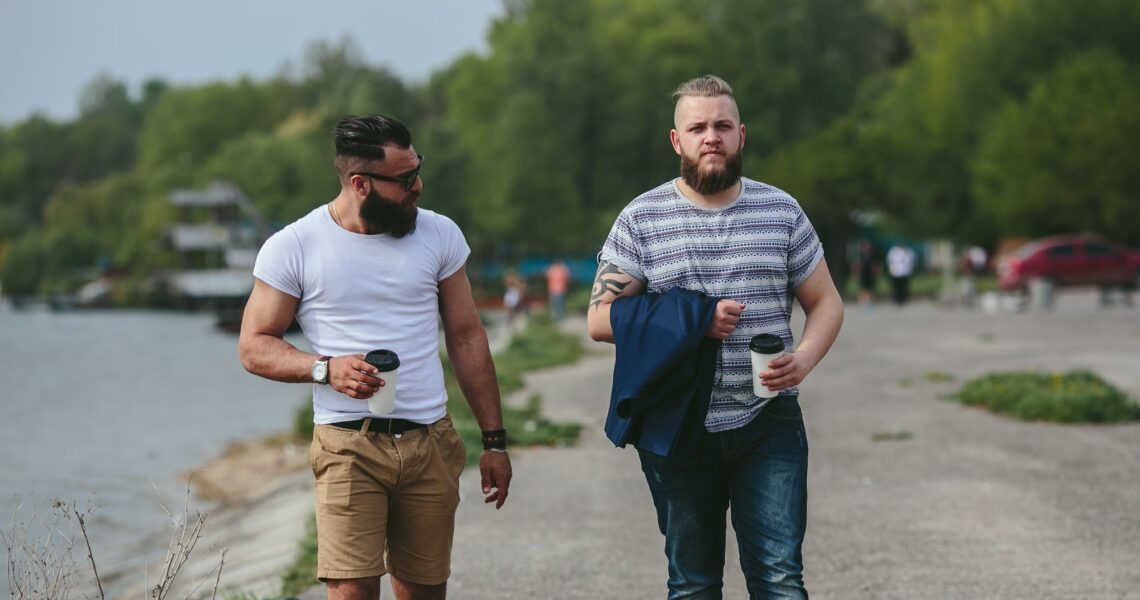 Two men walk and drink coffee
