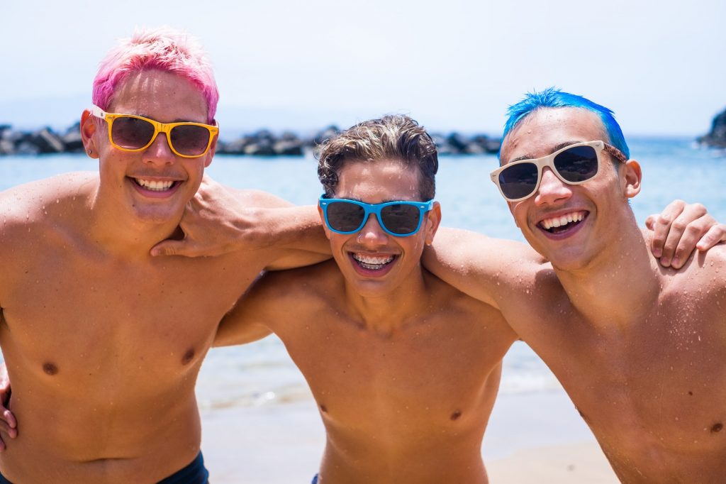 group of three friends having fun playing and enjoying together at the beach wearing sunglasses